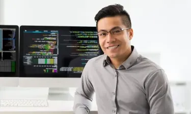 Computer programmer seated in front of two monitors showing coding software